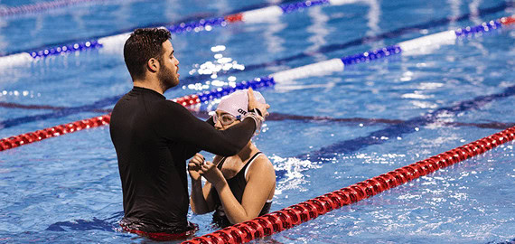 בבריכת שחייה גבר מסייע לשחיינית לחבוש כובע שחייה