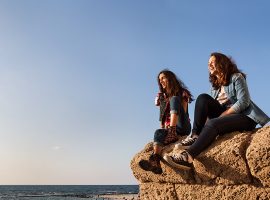 תצלום של שתי נשים יושבות על צוק ליד הים