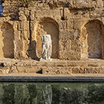 מבנה חלקי עתיק על שפת בריכת מים ובחזיתו פסל חסר ראש של אישה