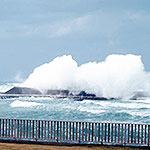 גלים נשברים על שובר גלים ומעלים קצף. בקדמת התמונה גדר על החוף.