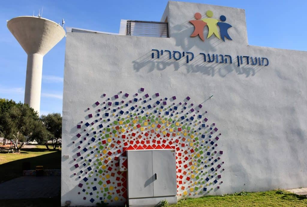 קיר חיצוני מקושט בצורות גאומטריות צבעוניות, בלוגו ובכיתוב: מועדון הנוער קיסריה.