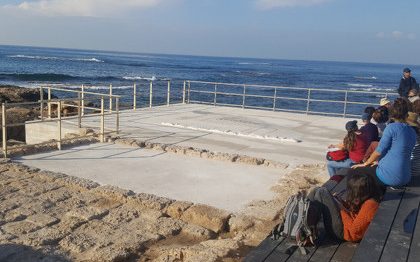 שרידי בית כנסת עתיק בקיסריה וקבוצת אנשים הכורעת לידם. ברקע הים
