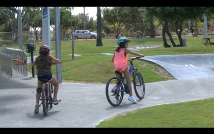 שתי ילדות רוכבות על אופניים בשביל מיוחד שנראה כי במכוון אינו מישורי. סביב השביל דשא ועצים.