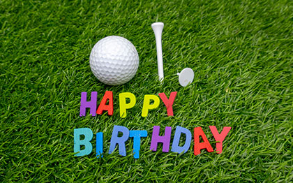 על כר הדשא מונחות אותיות צבעוניות היוצרות את הברכה: happy birthday, ומאחוריהן כדור גולף ואביזרי גולף נוספים