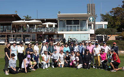 קבוצה גדולה של אנשים עומדים או כורעים לתמונה משותפת על הדשא ומאחוריהם בניין מועדון הגולף.