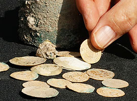 מטבעות עתיקים מונחים זה ליד זה ויד אוחזת באחד מהם