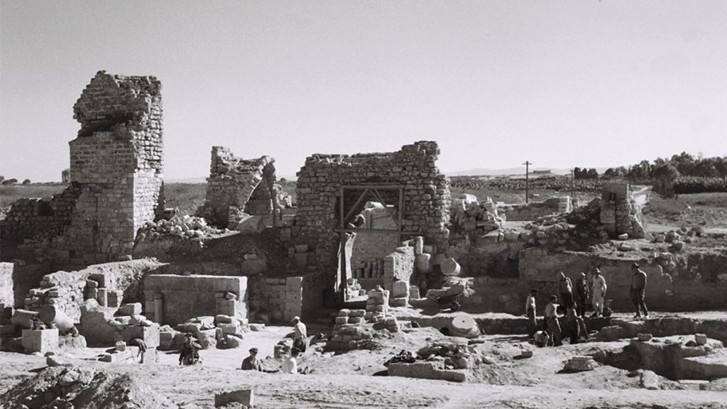 תצלום בשחור-לבן של שרידי מבנים מאבן ובהם קירות, עמודים, פתחים וקמרונות. חלק מהשרידים דו-קומתיים. בין השרידים נראים אנשים.