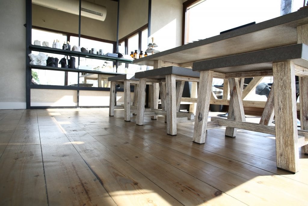 תצלום מנקודת מבט נמוכה של שולחן ושרפרפים מעץ וכן מדפים ועליהם מוצרי ספא