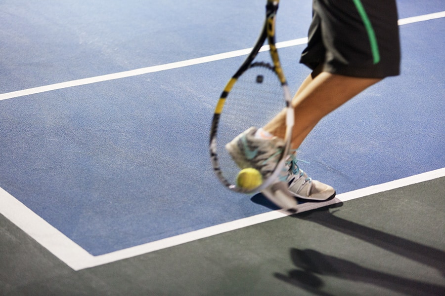 תצלום של מחבט טניס, כדור ורגליו של שחקן על מגרש טניס