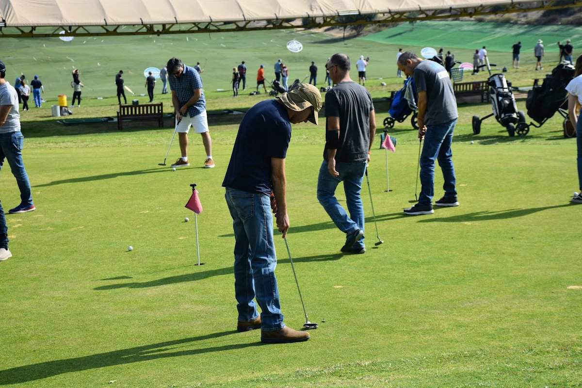 קבוצה גדולה של אנשים מתאמנים על הדשא במגרש גולף בשימוש במחבט.