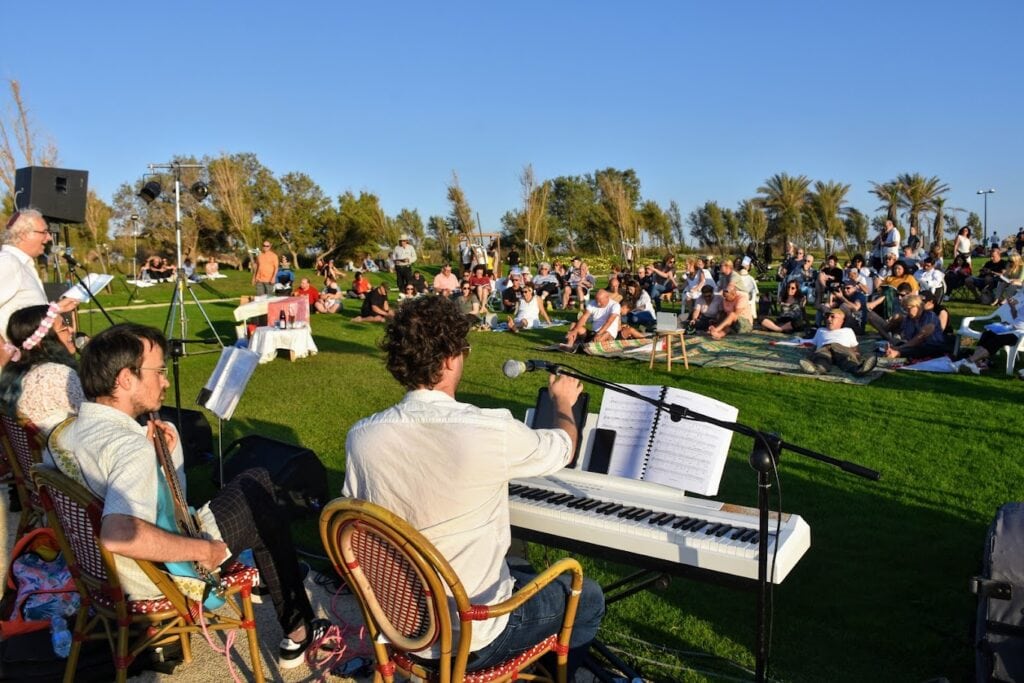 להקה מנגנת מול קהל שיושב בדשא בנמל קיסריה.