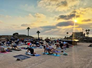 תיאור תווית ALT: קבוצת אנשים מתרגלים יוגה על חוף הים בקיס.